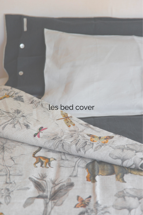 Dessus de lit avec une face avec des animaux de la jungle dessinés de façon naïve et douce et quelques touches de couleur orange sur fond blanc. L'autre face du dessus de lit est de couleur unie noire.